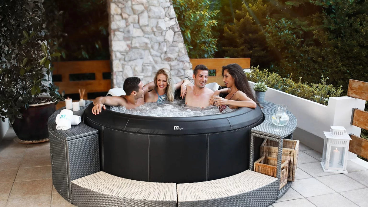 Round black inflatable spa with four adults relaxing on a patio, surrounded by wicker seating and decor