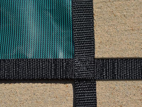 Close-up of green mesh safety pool cover with black webbing straps and step cutout detail