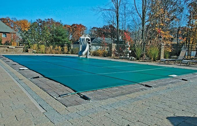 Green mesh safety cover stretched over a rectangular in-ground pool.